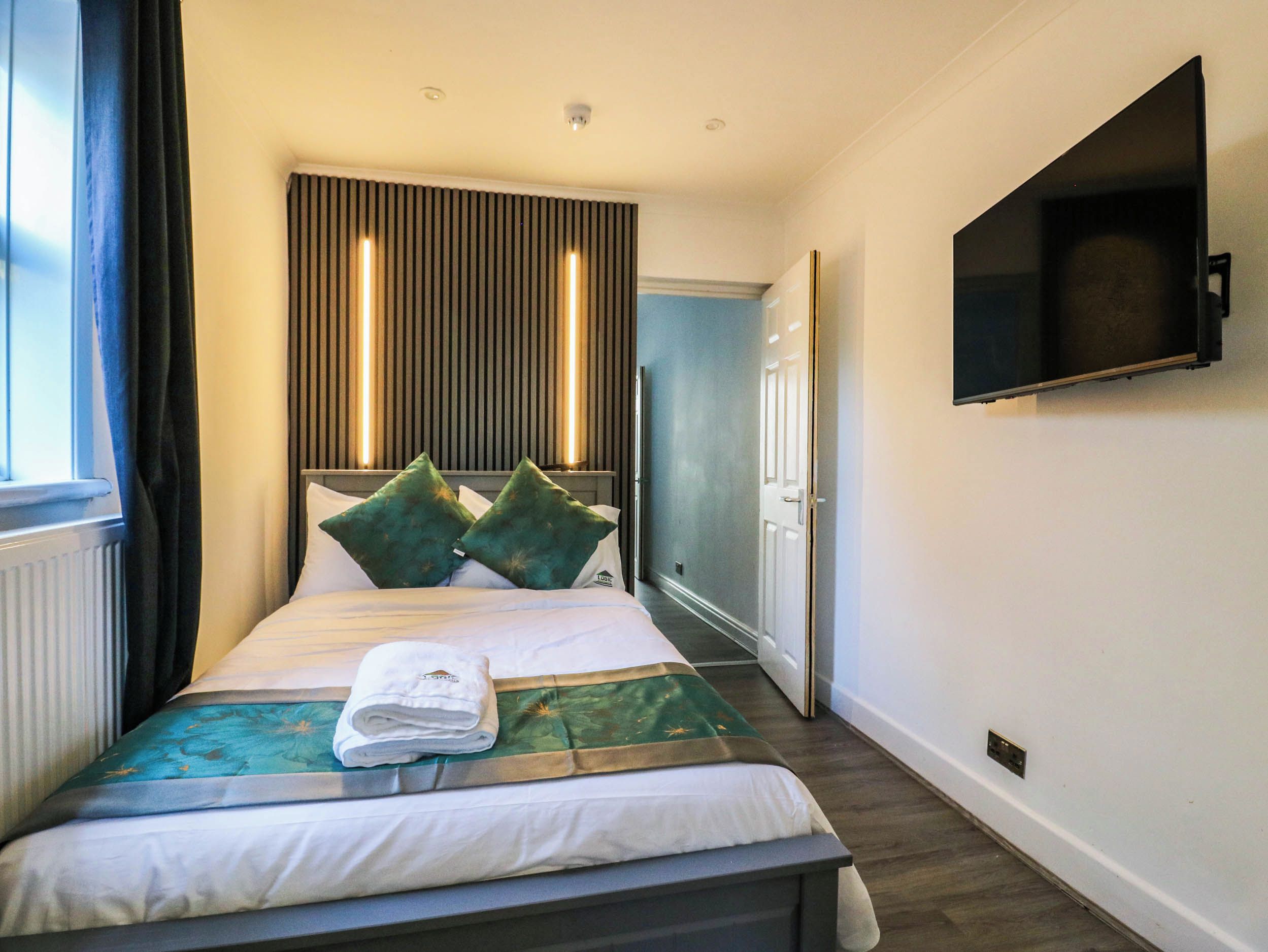 A hotel room with a bed, a flat-screen TV mounted on the wall, and a window with curtains.