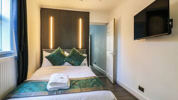A hotel room with a bed, a flat-screen TV mounted on the wall, and a window with curtains.