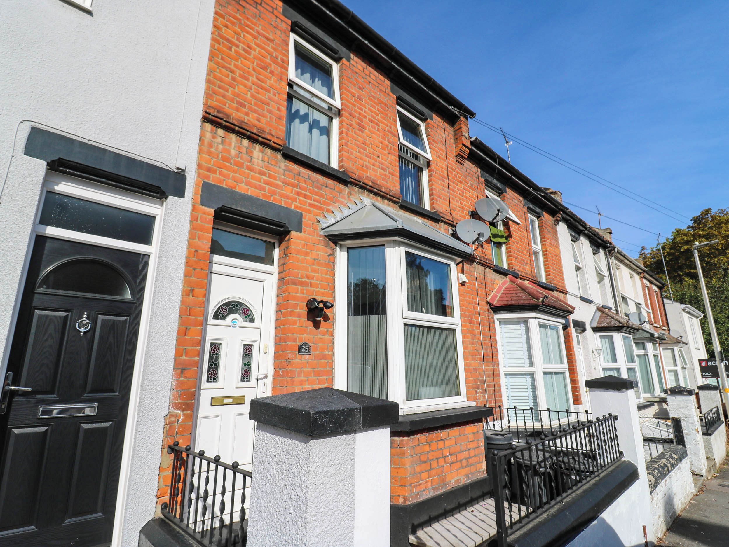 A row of terraced houses with distinct front doors, satellite dishes, and a clear blue sky.