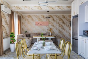 A modern dining area with a marble wall, a dining table set with white plates and gold chairs, and a kitchen with a stainless steel refrigerator. - Apartments Zarafshan city 151 Tashkent (Tashkent)