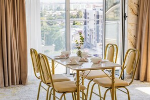 A dining area with a table set for four, four chairs, and a view of a cityscape through large windows. - Apartments Zarafshan city 151 Tashkent (Tashkent)