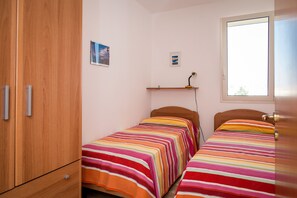 Un dormitorio con dos camas individuales, un armario de madera, un estante con una imagen y una ventana.