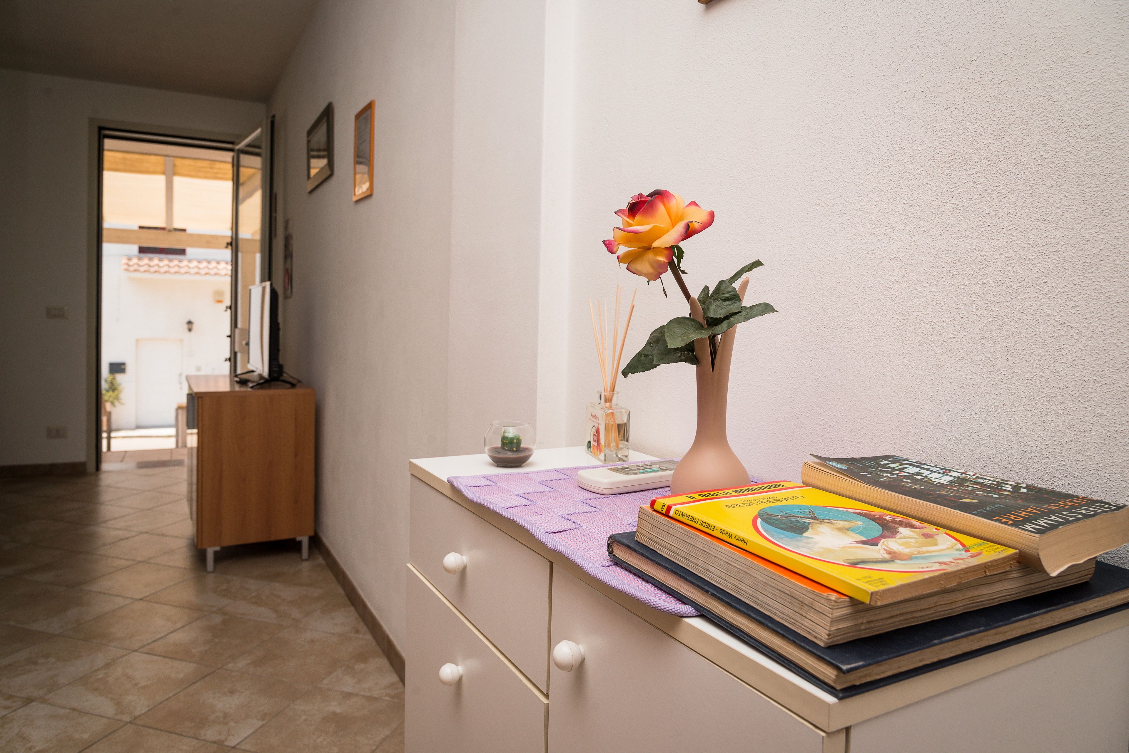 Une pièce avec un bureau, un vase contenant une seule fleur et une pile de livres.
