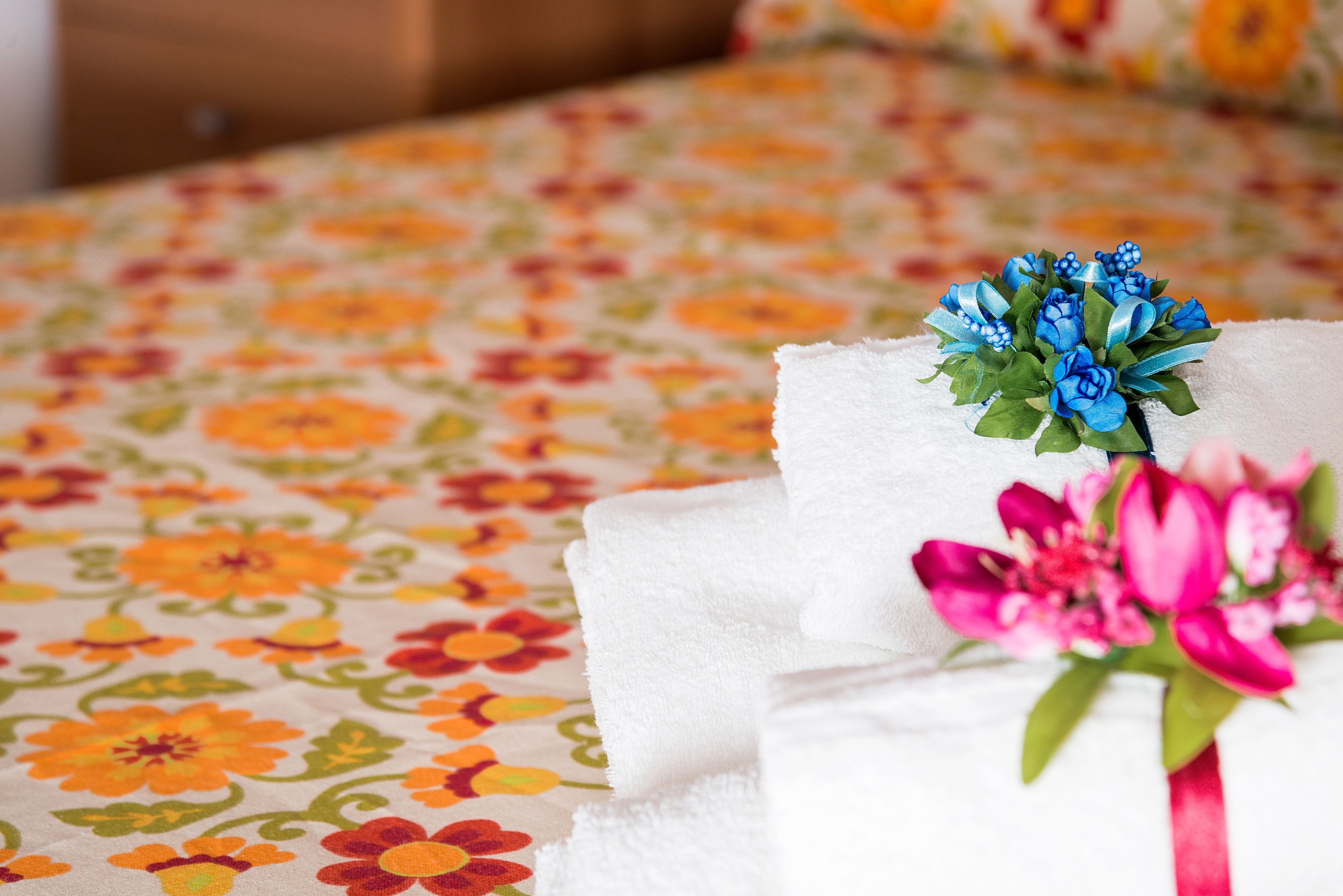 Une serviette blanche, soigneusement pliée, ornée d’un motif floral bleu et rose, est posée sur un lit recouvert d’une couvre-lit à motifs floraux.