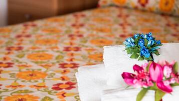 Une serviette blanche, soigneusement pliée, ornée d’un motif floral bleu et rose, est posée sur un lit recouvert d’une couvre-lit à motifs floraux.