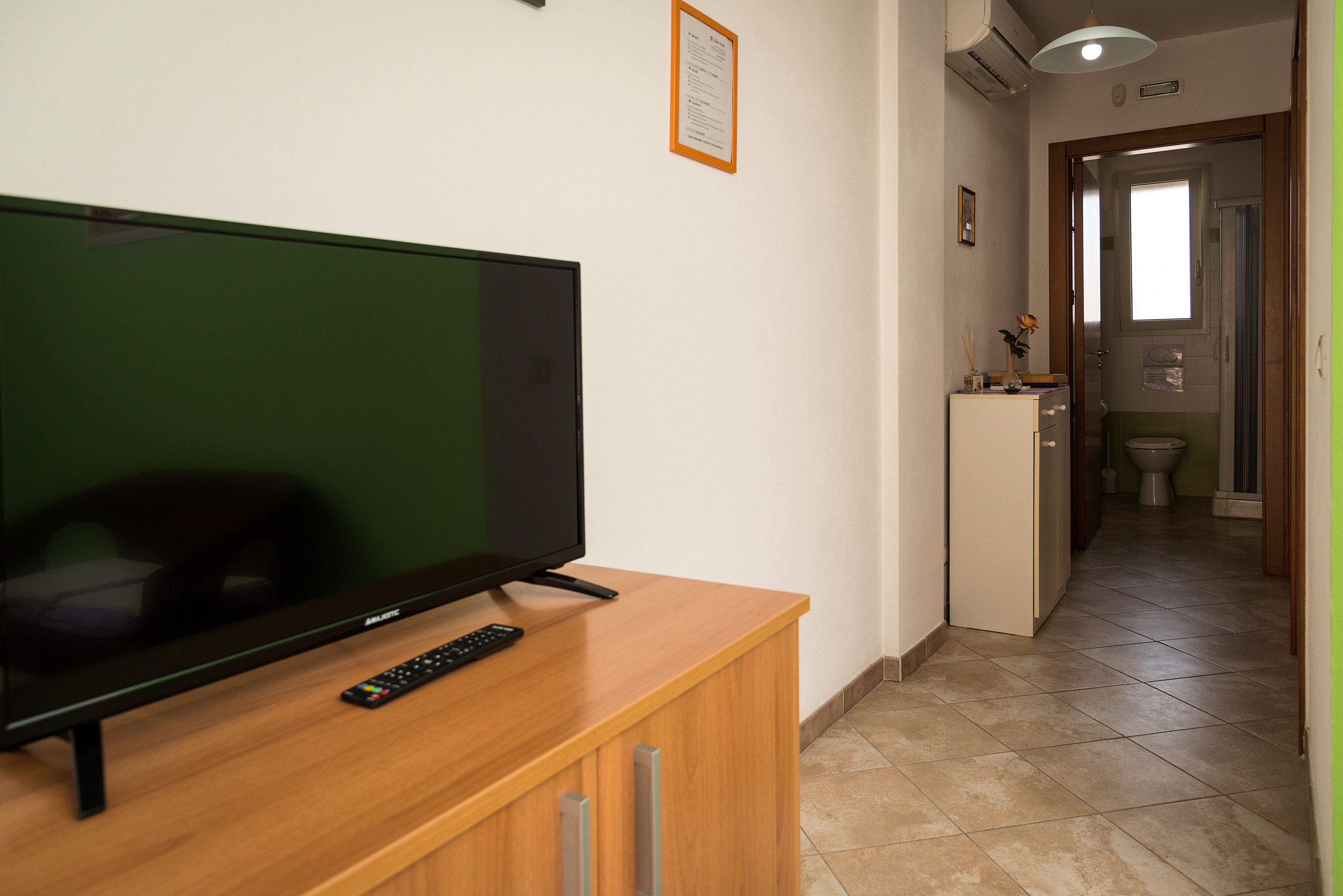 Une pièce avec un téléviseur posé sur un meuble en bois, une télécommande, un certificat encadré accroché au mur et une porte donnant sur une salle de bain.