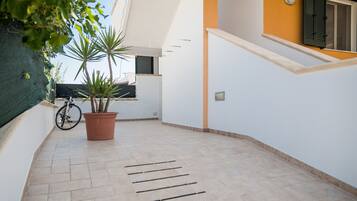A narrow corridor with a tiled floor, a potted plant, and a bicycle leaning against the wall.