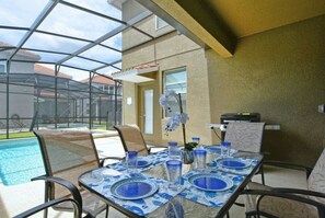 An outdoor patio with a glass enclosure, a pool, and a table set for dining. - 5BR Home Near Disney Pool & Mickey Room (Kissimmee)