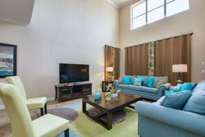 A living room with a television, a sofa, a coffee table, and a chair. - 5BR Home Near Disney Pool & Mickey Room (Kissimmee)