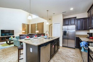 A modern kitchen with a central island, stainless steel appliances, and a dining area with a flat-screen TV. - 5BR Home Near Disney Pool & Mickey Room (Kissimmee)