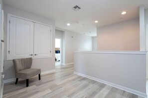 A room with a wooden floor, a chair, a white door, and a white wall. - 6BR Sonoma Resort Home Pool & Cars Game Room (Kissimmee)