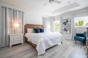 Een slaapkamer met een groot bed, nachtkastjes, een plafondventilator en kunst aan de muur.