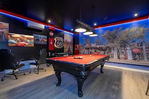 Een pooltafel met een rode viltbekleding, omringd door zwarte stoelen en een biljartkeu.