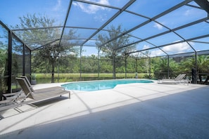 An outdoor swimming pool with a glass enclosure, surrounded by lounge chairs and a view of a natural landscape. - 6BR Sonoma Resort Home Pool & Cars Game Room (Kissimmee)