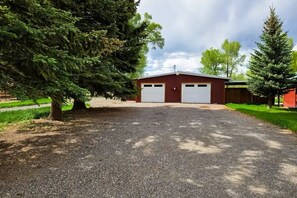 A gravel driveway leading to a red building with two white garage doors. - Pioneer Ridge Apartment | Del Norte Mtn Getaway (Del Norte)