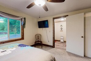 A bedroom with a bed, a ceiling fan, a TV mounted on the wall, and a window with a view of greenery. - Pioneer Ridge Apartment | Del Norte Mtn Getaway (Del Norte)