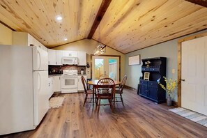 Eine Küche mit Holzbalkendecke, weißen Schränken, einem Esstisch mit Stühlen und einem dunklen Schrank.