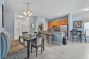 A modern kitchen with wooden cabinets, a central island, and a dining area with a table and chairs. - 5BR Nemo Room Townhouse Pool, 10min Disney (Kissimmee)