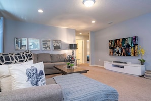 A living room with a sofa, coffee table, and a flat-screen TV mounted on the wall. - 6BR Near Disney Private Pool, Spa, Movie Room (Kissimmee)
