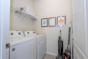 A laundry room with two front-loading washing machines, a drying rack, and three framed laundry charts on the wall. - 6BR Near Disney Private Pool, Spa, Movie Room (Kissimmee)