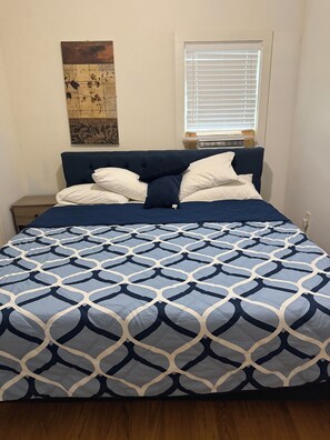 Ein Bett mit einem geometrisch gemusterten Überwurf, einem Kopfteil und einem Nachttisch mit einer Lampe.