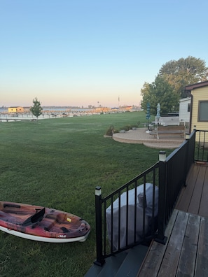 Ein Garten mit Rasen, einem Kajak, einer Terrasse und Blick auf ein entferntes Gewässer.