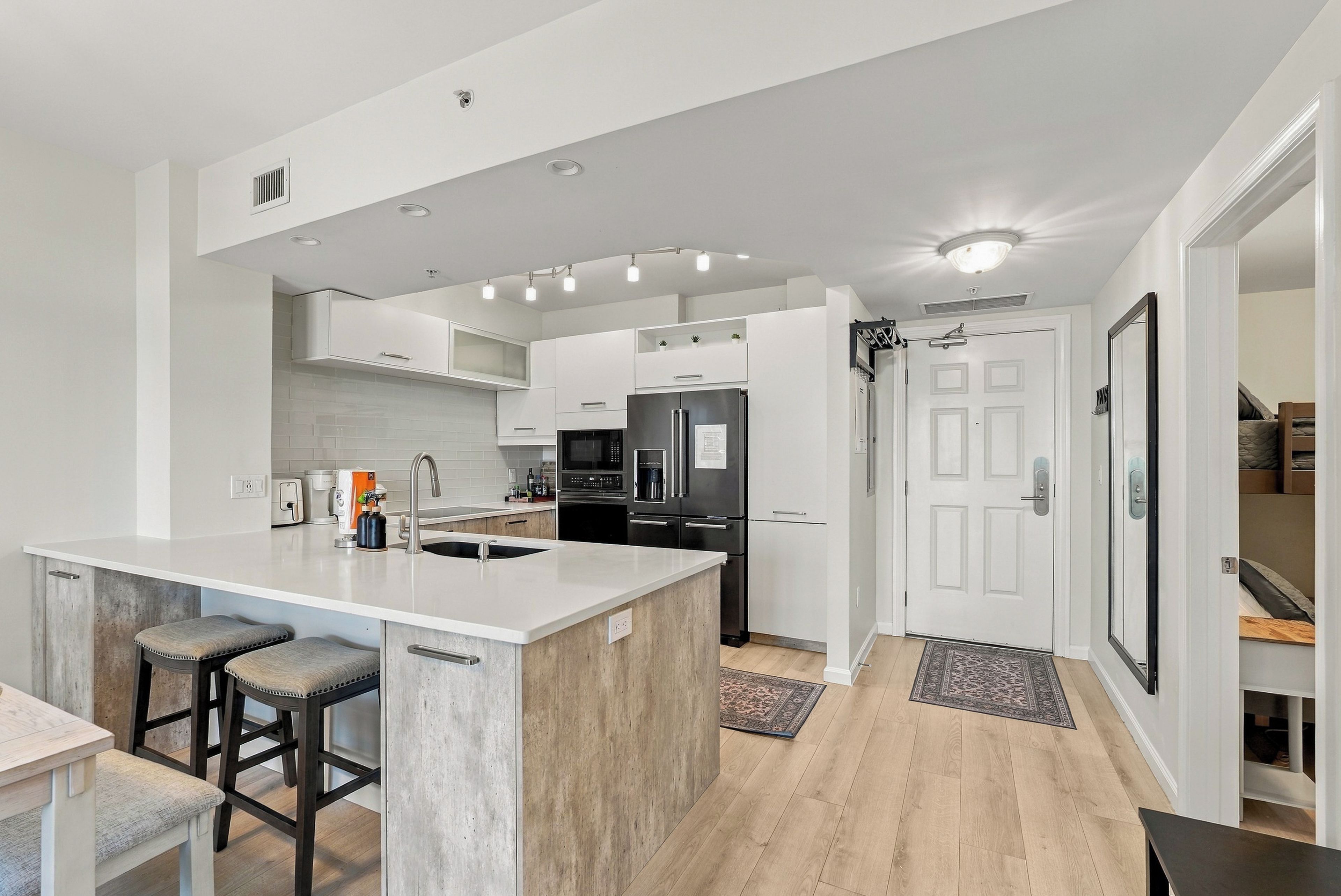 A modern kitchen with a central island, bar stools, a refrigerator, and a microwave.