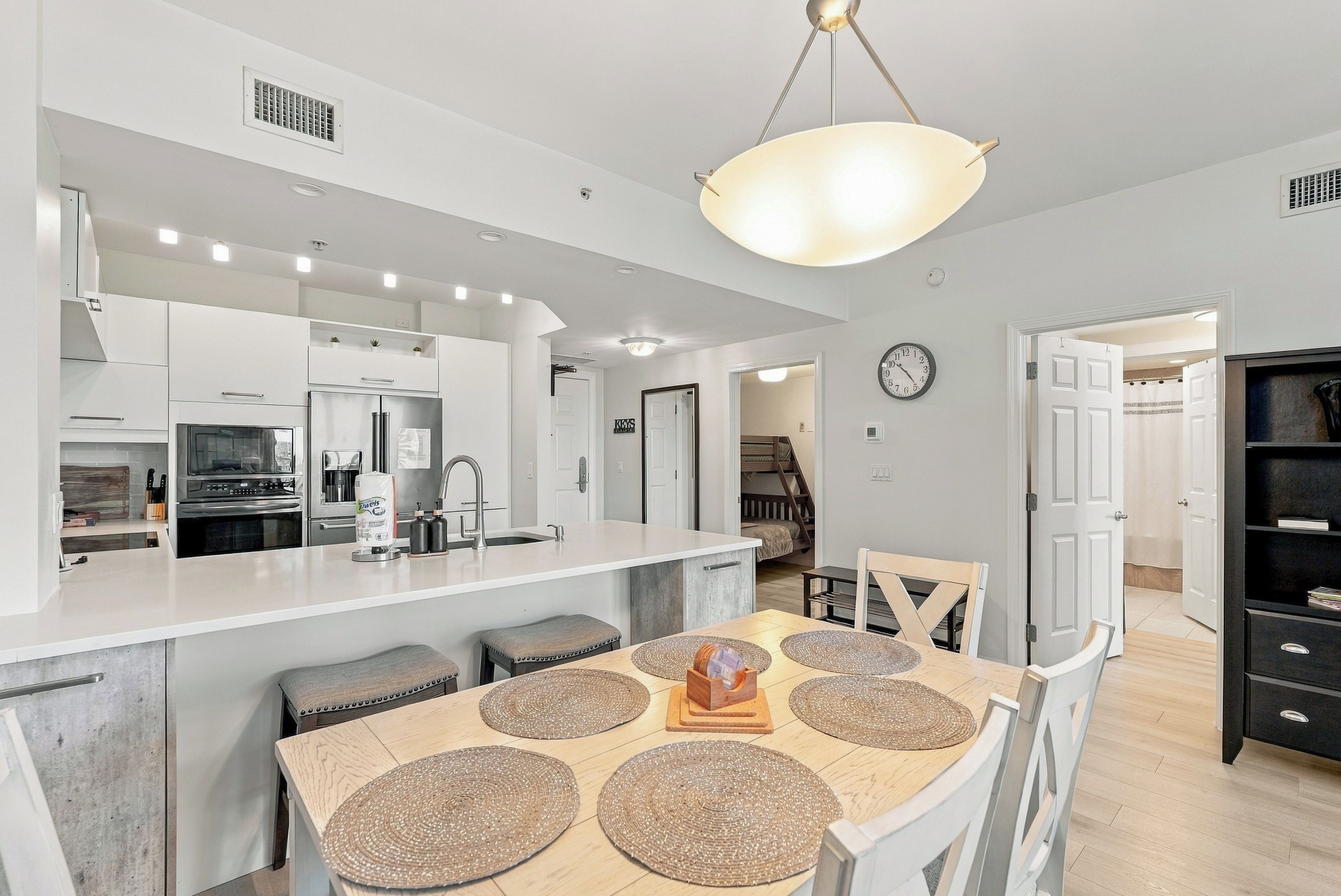 A modern kitchen with a central island, stainless steel appliances, and a dining area with a wooden table and woven placemats.