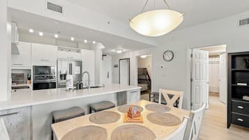 A modern kitchen with a central island, stainless steel appliances, and a dining area with a wooden table and woven placemats.