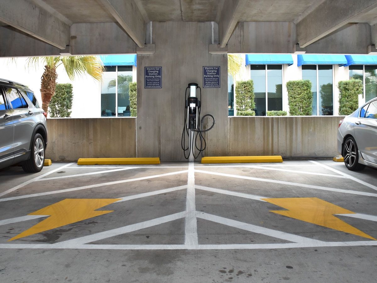 An underground parking area with electric car charging stations, marked parking spaces, and directional arrows on the floor.