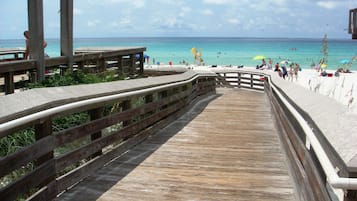 A wooden boardwalk leading to a beach with clear turquoise water and a sandy shore.