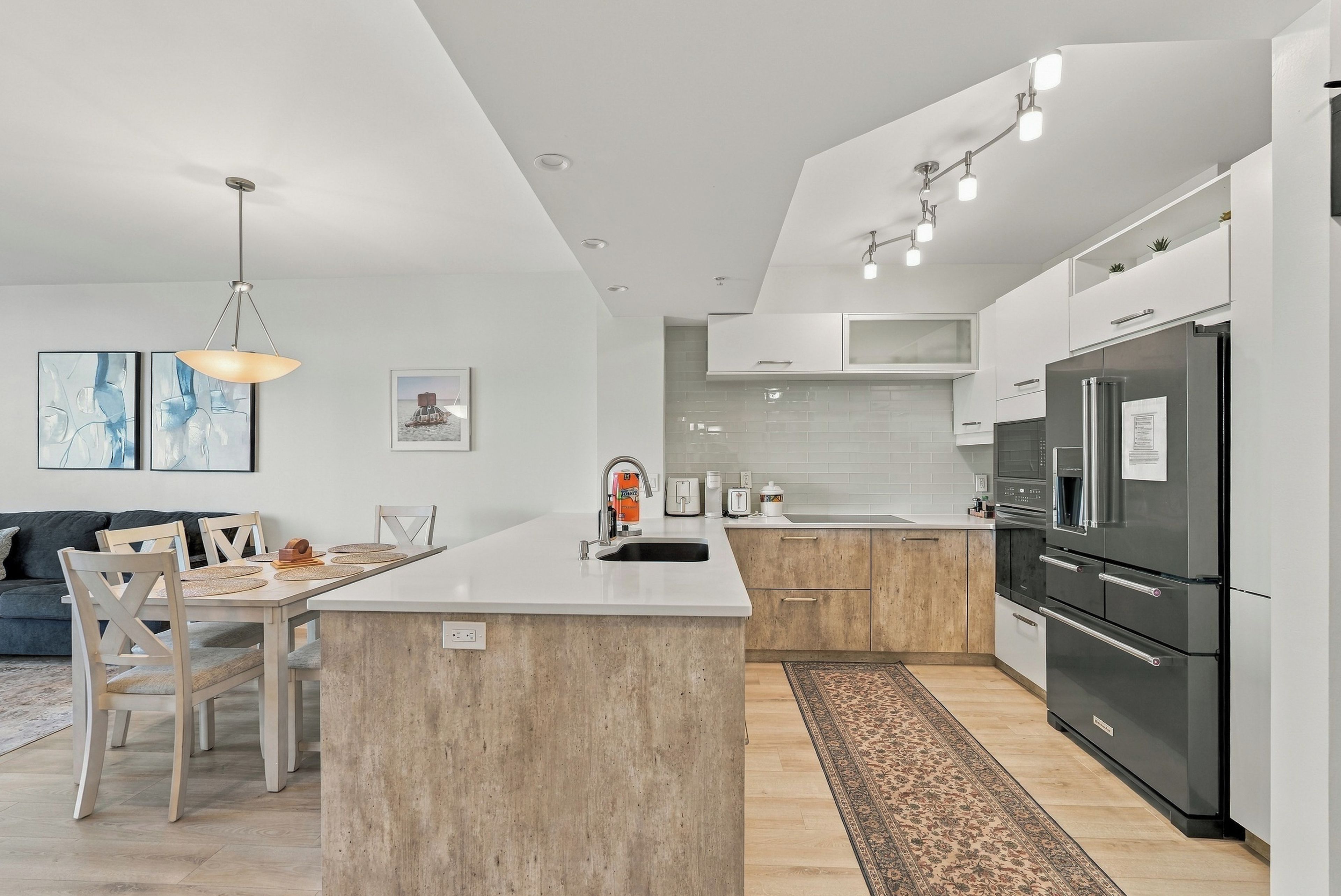 A modern kitchen with a central island, stainless steel appliances, and a dining area with a sofa and chairs.