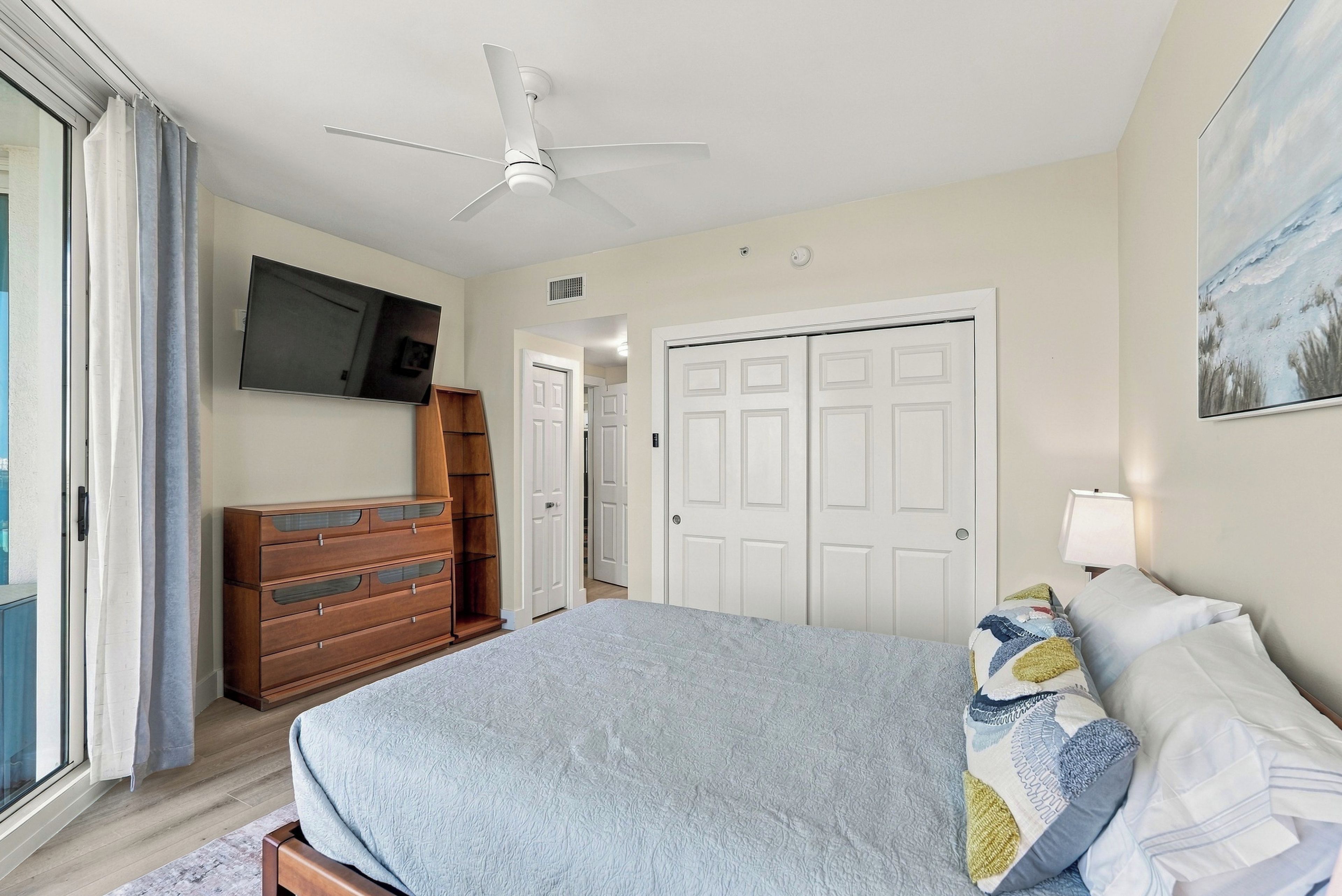A bedroom with a bed, a TV, a ceiling fan, and a wardrobe.