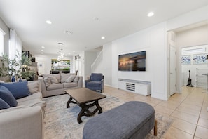 Ein modernes Wohnzimmer mit Sofa, Sessel, Couchtisch und einem an der Wand montierten Fernseher.
