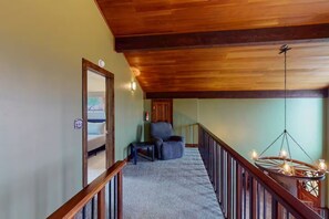 A spacious loft bedroom with a high ceiling, a large window, and a cozy seating area with a chair and a small table. - 4BR Home + Apt. w/ Mountain Views, near Wolf Creek (Del Norte)