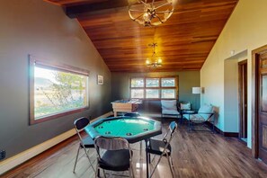 A pool table with four chairs, a foosball table, and a ceiling fan in a room with wooden flooring and large windows. - 4BR Home + Apt. w/ Mountain Views, near Wolf Creek (Del Norte)