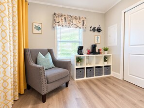 Ein gemütliches Wohnzimmer mit einem grauen Sessel, einer Kaffeestation und einem Bücherregal.