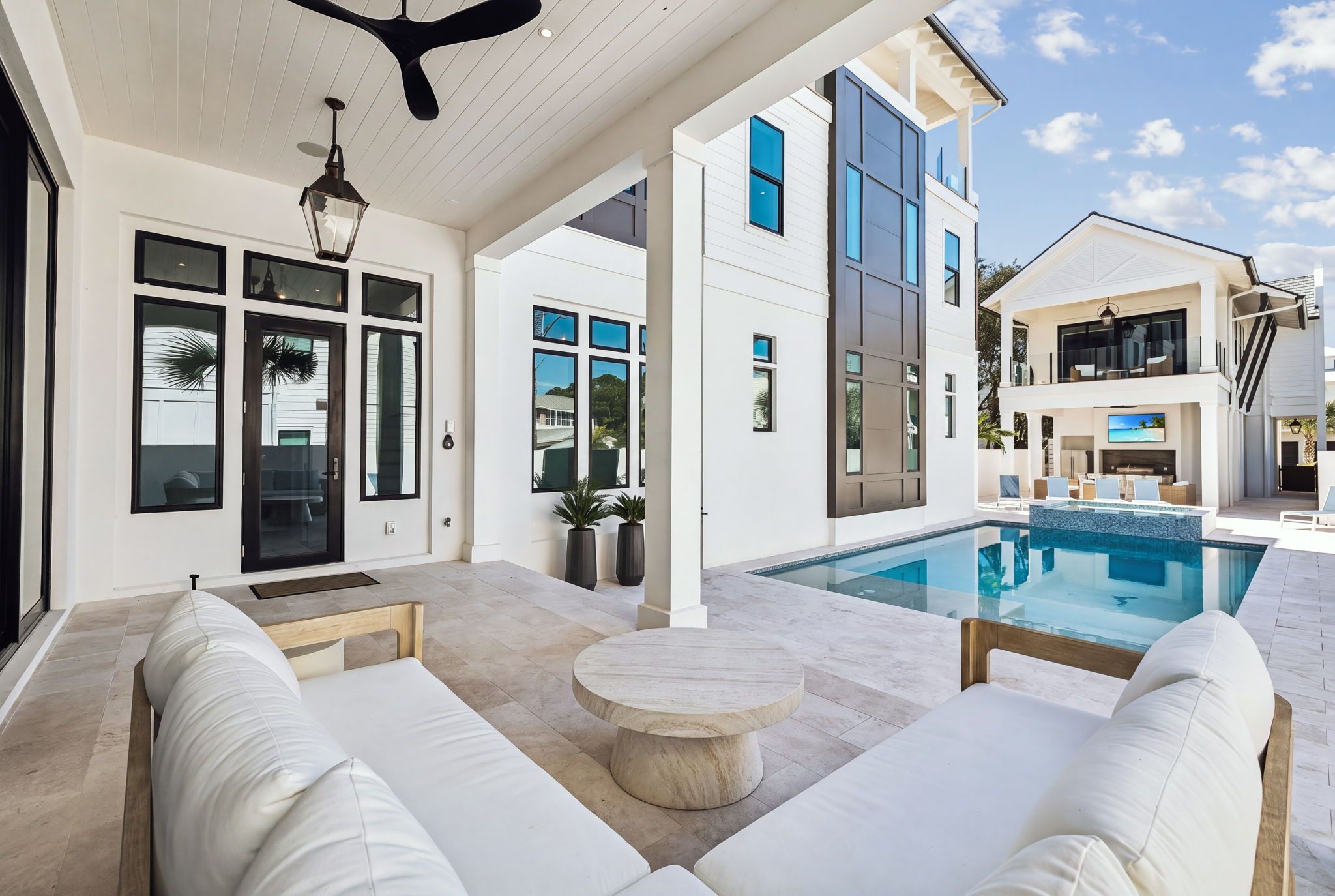 A modern outdoor living area with a pool, white furniture, and a clear sky.