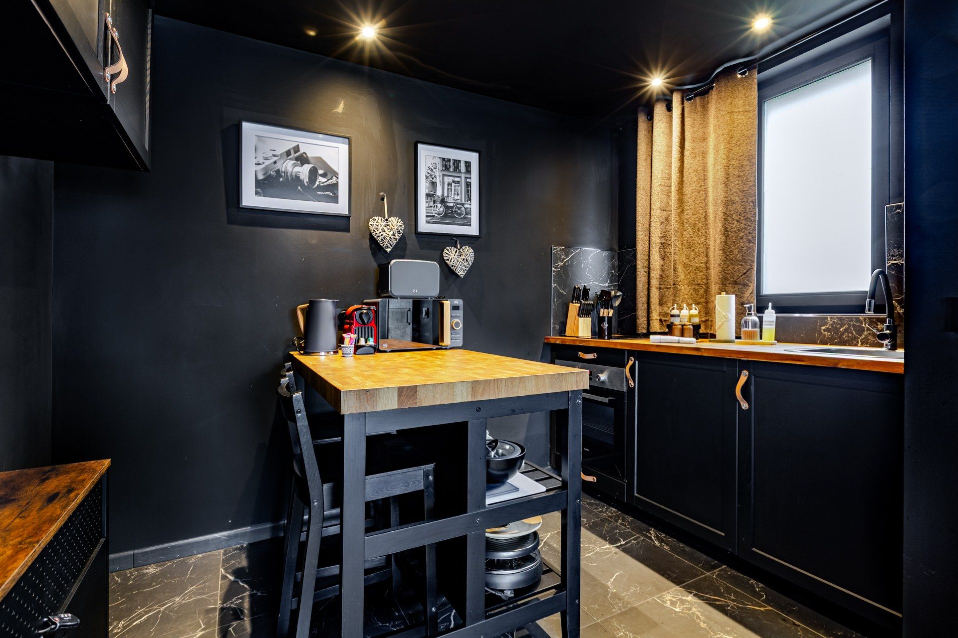 A compact kitchen with a wooden table, black cabinets, and a window with curtains.