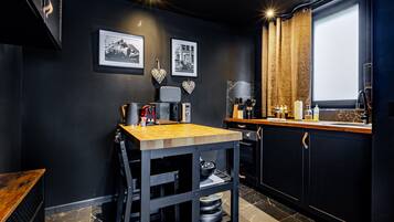 A compact kitchen with a wooden table, black cabinets, and a window with curtains.