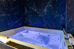 A bathtub with a white interior, set against a dark blue marble wall with white veins.