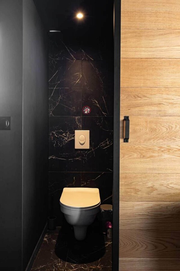 A modern bathroom with a marble wall, a wooden panel, a toilet, and a light switch.