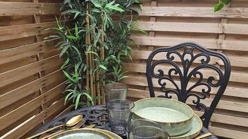 A round table with plates, glasses, and cutlery, set against a wooden backdrop with a bamboo plant.