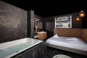 A modern bathroom with a marble wall, a bathtub, a wooden vanity, and a bed with a headboard.