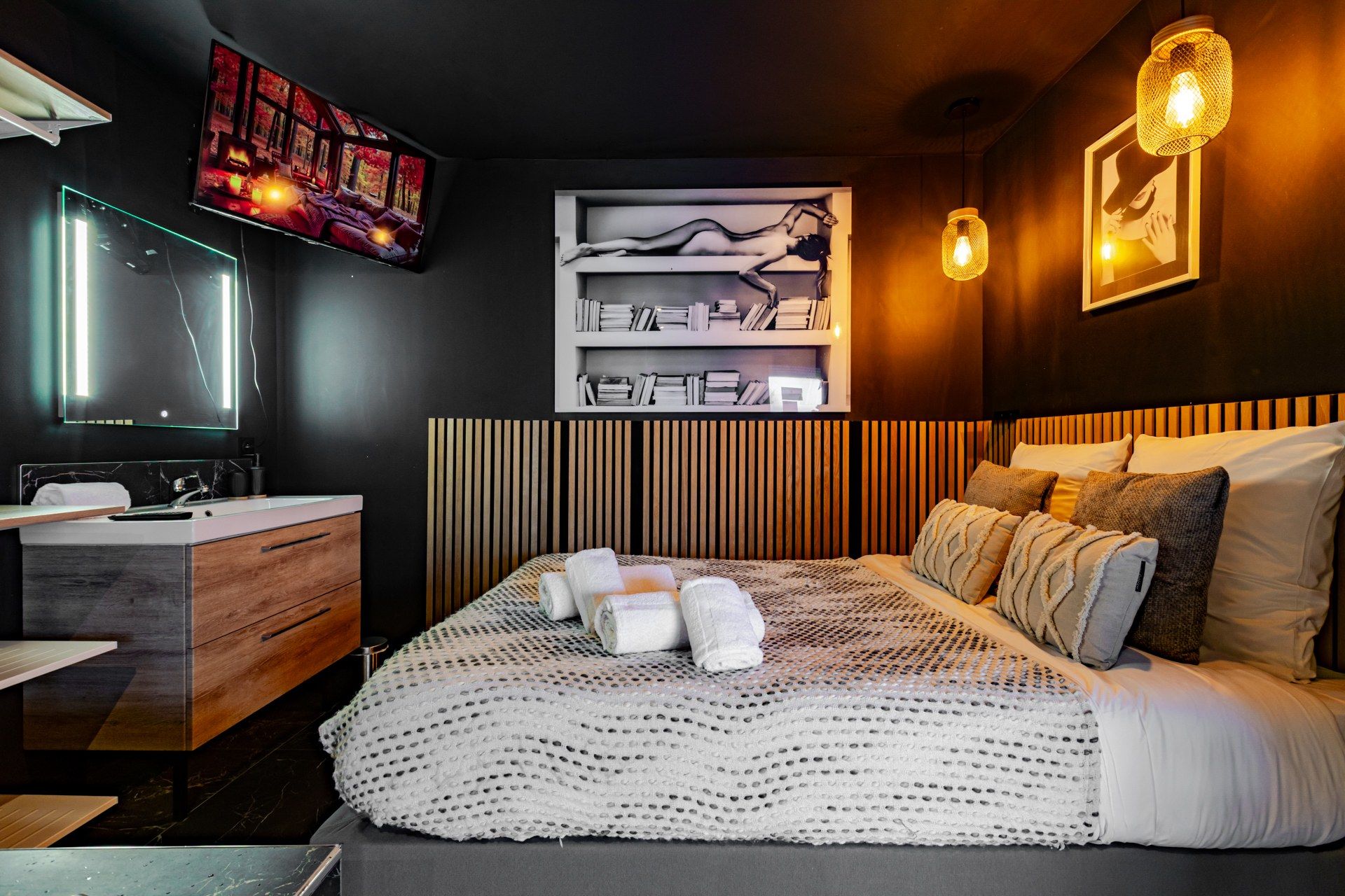 A modern bedroom with a large bed, a bedside table, a mirror, a TV, and a bookshelf.
