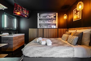 A modern bedroom with a large bed, a bedside table, a mirror, a TV, and a bookshelf.