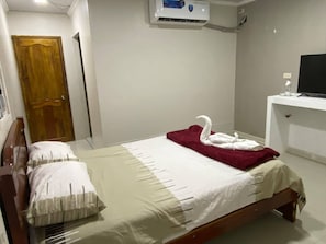 Una habitación de hotel con una cama, una puerta de madera, una pared blanca y un equipo de aire acondicionado blanco.