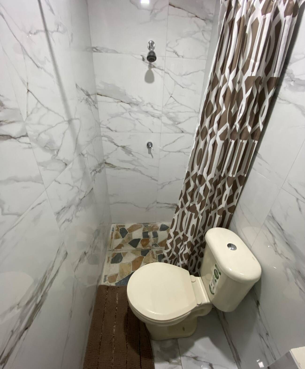 Un baño con inodoro, ducha y paredes de mármol.