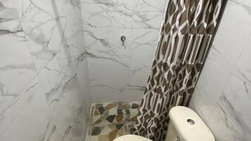 Un baño con inodoro, ducha y paredes de mármol.