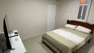 A bedroom with a bed, a desk with a computer, and a window.